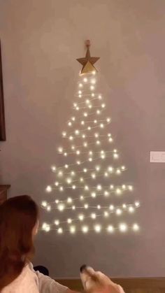 a woman sitting in front of a christmas tree with lights on it and a dog laying next to her