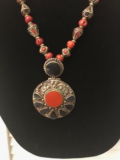 A large and truly dramatic pendant of black onyx and coral accompanies a varying array of Nepalese brass beads inlaid with black onyx and coral interspersed with Sherpa glass beads and Nepalese brass spacers. The total length of this necklace extends to 28.75 " long, but can be adjusted to be a short as 26" long. Handmade Black Carnelian Necklace, Black Carnelian Jewelry With Natural Stones, Handmade Black Carnelian Jewelry, Bohemian Onyx Beaded Necklace With Black Beads, Bohemian Onyx Round Bead Jewelry, Traditional Red Beads With Natural Stones, Black Bohemian Medallion Jewelry, Traditional Bronze Jewelry With Natural Stones, Bohemian Onyx Necklace With Black Beads