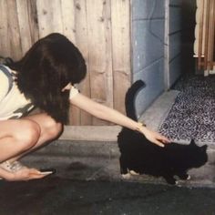 a woman kneeling down petting a black cat