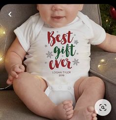 a baby sitting on a couch wearing a white bodysuit with the words best gift ever printed on it