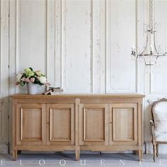 a wooden cabinet sitting in front of a white wall with flowers on top and a chandelier hanging from the ceiling