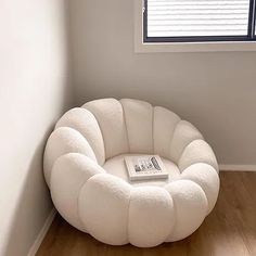 a white chair sitting in front of a window next to a book on a wooden floor