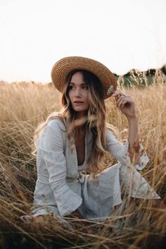 a woman sitting in tall grass wearing a hat