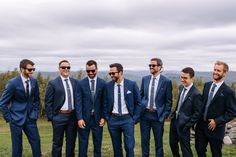 a group of men standing next to each other wearing suits and sunglasses on top of a grass covered field