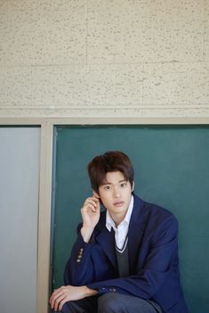 a young man in a blue suit sitting on a chair talking on a cell phone