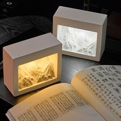 an open book sitting on top of a wooden table next to two illuminated cubes