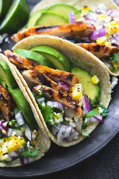 three tacos with chicken, avocado and cilantro on a plate