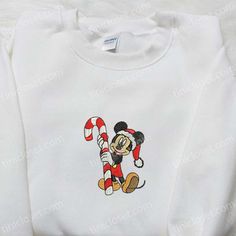 Mickey Candy Cane Embroidered Shirt, Disney Characters Embroidered Hoodie, Best Christmas Gifts For Family Welcome to Tinicloset, where we turn ordinary clothing into delightful canvases of imagination and style. Our store is a treasure trove of enchanting apparel, a place where threads come to life with whimsy and wonder. Get ready to embark on a journey of curiosity and excitement as we unveil our collection of custom embroidered garments that will surely tickle your fancy. At Tinicloset, we&# Disney Sweatshirts Christmas, Christmas Disney Sweatshirt, Christmas Disney Hoodies, Disney Xmas Sweaters, Disney Christmas Sweatshirts & Hoodies, Maroon Hoodie, Hoodie Material, Blue Sweatshirt, Christmas Hoodies