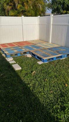 a backyard area with concrete blocks laid out in the grass and a white fence behind it