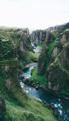 a river flowing through a lush green valley surrounded by tall rocky cliffs and grass covered hillsides