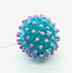 a blue and pink beaded ball on a white surface with wires in the background