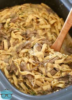 a pot filled with pasta and meat on top of a wooden spoon