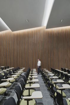 an empty room with rows of desks and chairs in front of a wooden wall