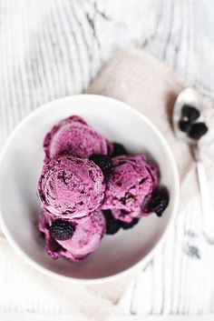 a white bowl filled with blueberry ice cream on top of a table next to a spoon