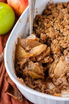 an apple crisp in a white dish next to apples