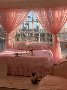 a cat sitting on the floor in front of a bed with pink sheets and drapes