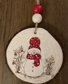 a snowman ornament is hanging on a wood slice with red and white beads