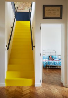 there is a yellow stair case in the hallway next to a bed and pictures on the wall