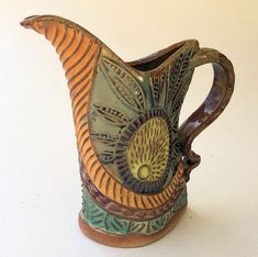 a ceramic pitcher with an intricate design on the front and sides, sitting on a white surface