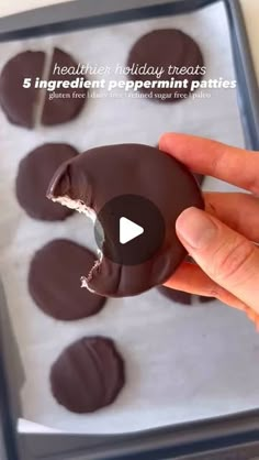 a hand holding a chocolate covered donut in front of a pan full of doughnut holes