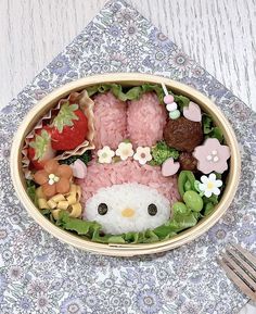 a bowl filled with hello kitty food on top of a floral table cloth next to a fork and knife