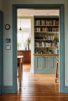 an open door leading to a kitchen with bookshelf and table in the background