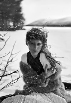 black and white photograph of a woman sitting in the snow with her hair blowing in the wind