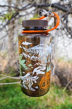 a glass jar hanging from a tree with an orange handle and some drawings on it