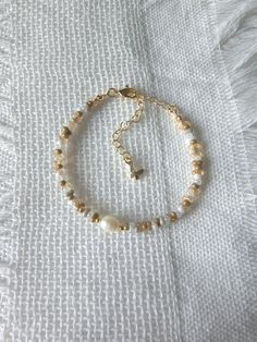 a bracelet with gold beads and a cross on the clasp is laying on a white sheet