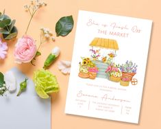 a card with flowers and an umbrella next to it on a pink tablecloth, surrounded by greenery