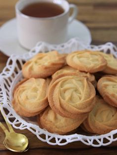 a white plate filled with cookies next to a cup of tea and gold spoons