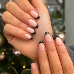 a woman's hands with black and pink nail polish on her nails next to a christmas tree