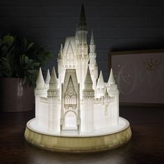 an illuminated castle sits on a table next to a potted plant