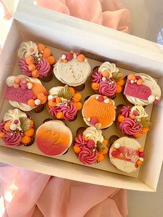 a box filled with lots of cupcakes on top of a pink table cloth