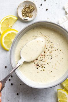 a hand holding a spoon over a bowl of creamy cheese dressing with lemons around it