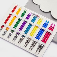 six different colored pens sitting in a holder next to a white card with a cloud on it