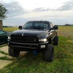 a black truck parked on top of a grass covered field next to a green car