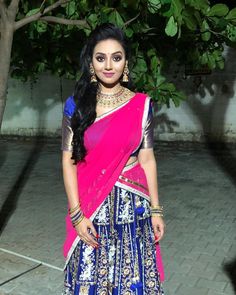 a woman in a blue and pink lehenga standing on a brick floor next to a tree