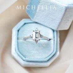 an engagement ring in a blue box on a white cloth covered surface with a diamond center stone