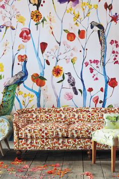 a couch and two chairs in front of a wall with colorful floral designs on it