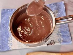 a spoon is stirring chocolate in a pot on a table with a blue napkin and wooden utensils