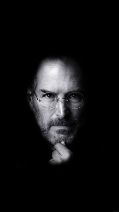 a black and white photo of steve jobs looking at the camera with his hand on his chin