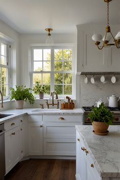 a white kitchen with marble counter tops and gold accents on the windowsills is pictured