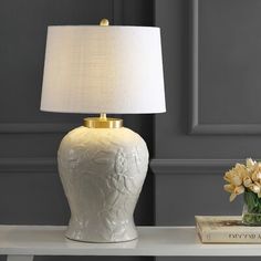 a white table lamp sitting on top of a desk next to a vase with flowers