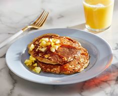 two pancakes on a plate with syrup and honey next to it, along with a glass of orange juice