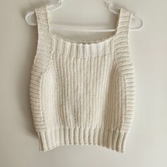 a cropped sweater hanging on a hanger against a white wall with no clothes