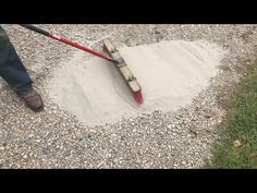 a man is shoveling sand in the ground with a red handled broom on it