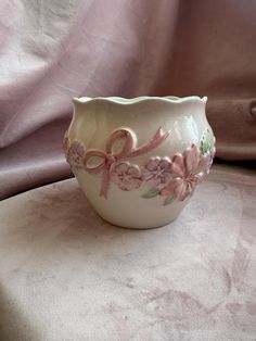 a white bowl with pink flowers on it sitting on top of a cloth covered table