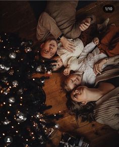 three people laying on the floor next to a christmas tree