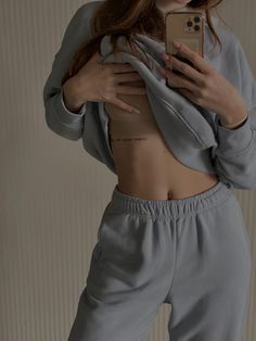 a woman taking a selfie with her cell phone while wearing grey sweatpants and crop top